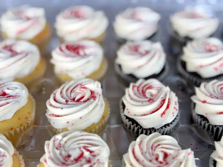 A tray of chocolate and vanilla cupcakes with white frosting sprinkled with red sugar